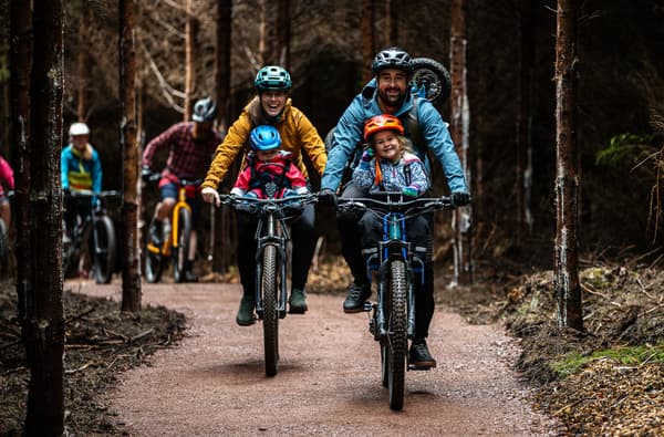 Family cycling through the forest on a cycling path in the Forest of Dean photo credit Forestry England